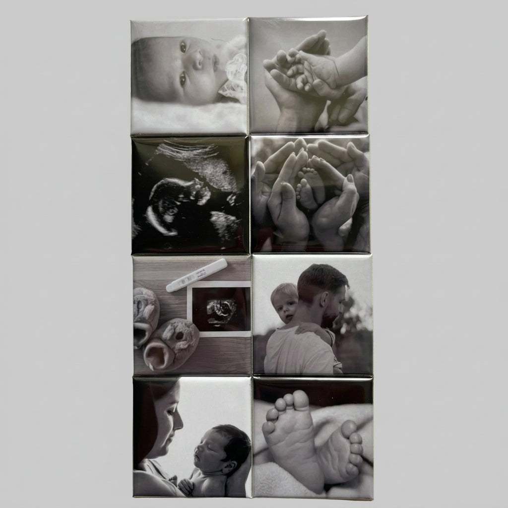 A set of nine square ceramic tiles arranged in a 3x3 grid, featuring black and white photographs of babies, hands, ultrasound images, and tender moments. The tiles are displayed on a textured beige fabric background.