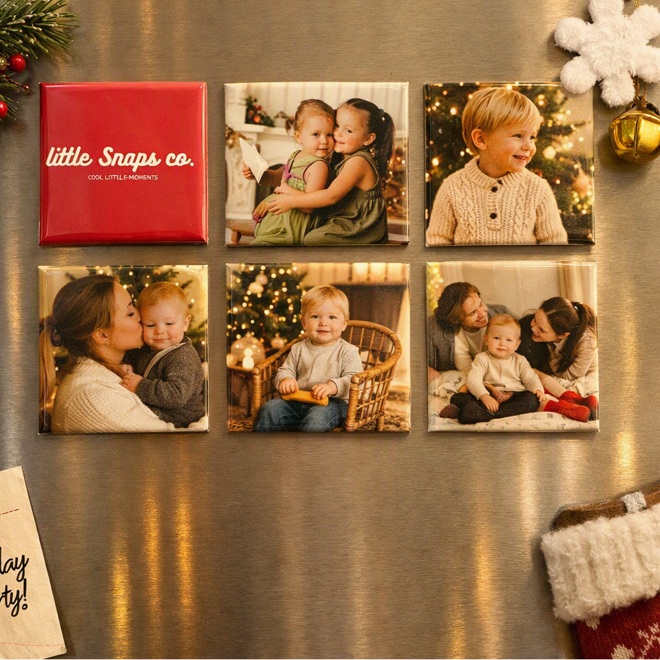 Six christmas photo magnets arranged on a stainless steel refrigerator, holiday-themed props including a green pine branch, white fluffy ornament, gold ornament, and a Christmas stocking corner.